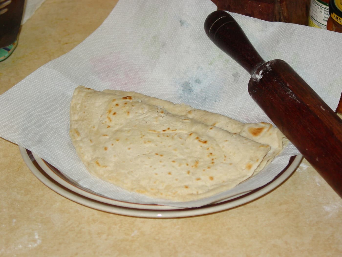 A freshly made Guyanese roti on a plate beside a rolling pin