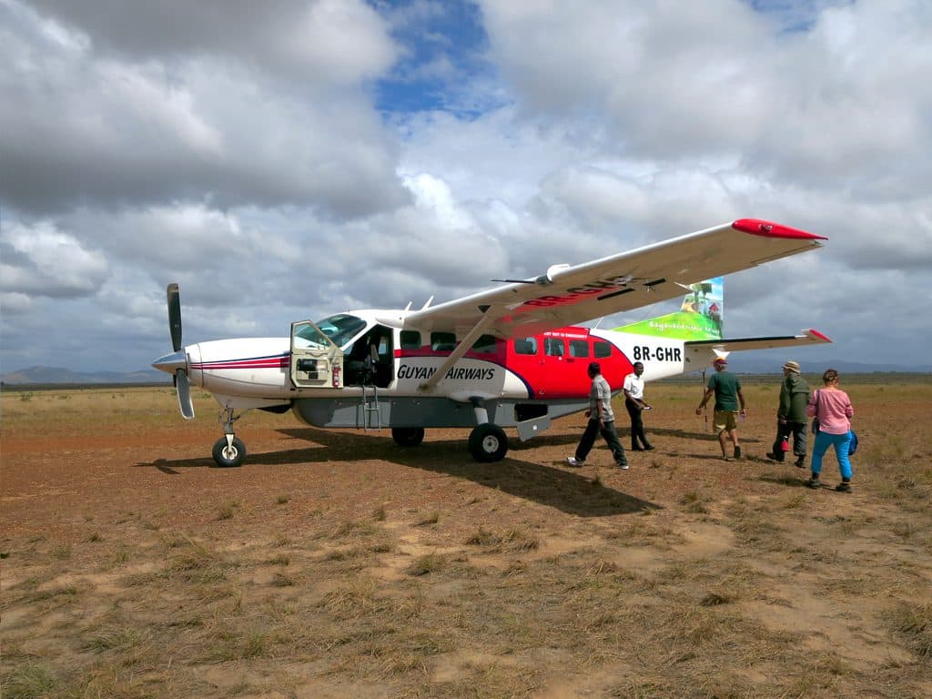 Passengers walking away from a small Trans Guyana Airways aircraft on a savannah airstrip
