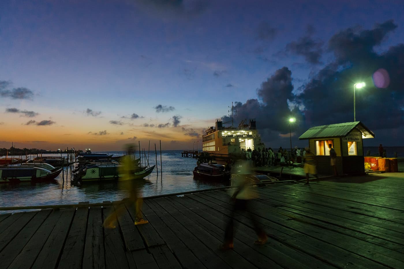 The river stelling at Parika at dusk, with boats moored and people walking on the wooden deck