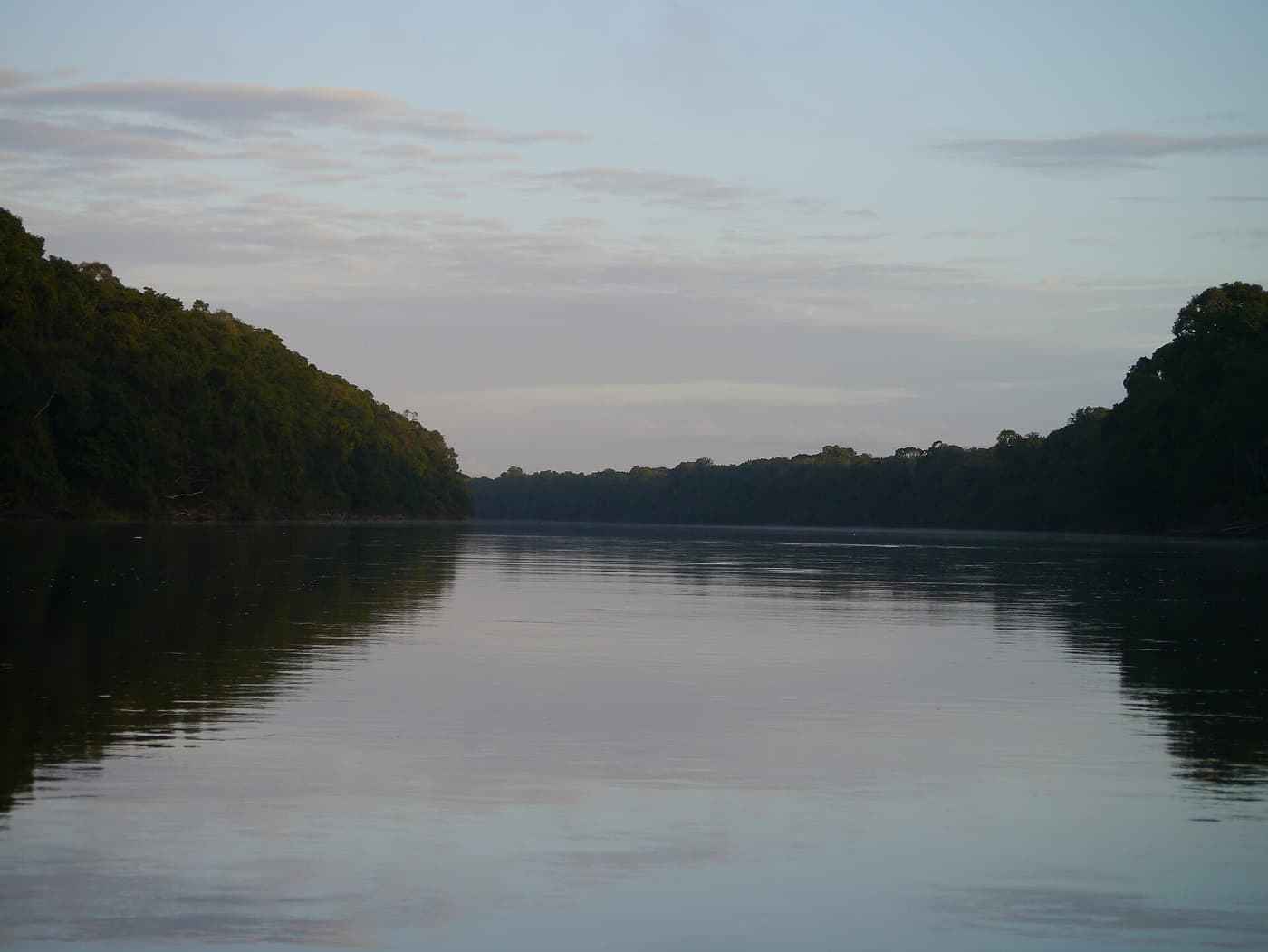 A calm forest-lined river reflecting the sky at dusk