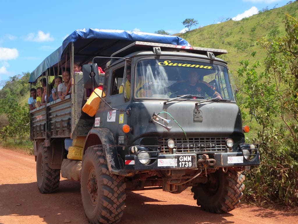 An open-backed Bedford truck carrying passengers along a red dirt road